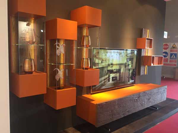 میز زیر تلویزیونی مدرنی با رنگ نارنجی در تصویر می باشد که بر روی دیوار نصب شده است و قفسه های آن به صورت مجزا و بسته شیشه ای می باشد و صفحه نمایشگر در مرکز آن قرار گرفته است.