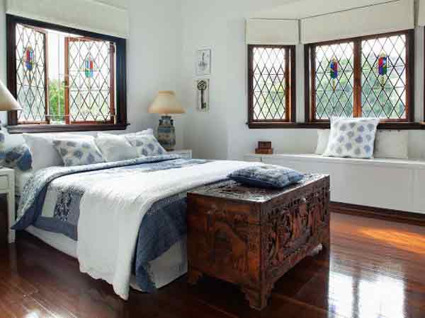 تصویر یک اتاق خواب را نشان می دهد که دارای یک تخت دو نفره با تم سفید آبی می باشد و کنار تخت دو میز عسلی سفید قرار گرفته است که رو آن ها یک آباژور طرح دار می باشد و بالای تخت یک پنجره چوبی طرح دار به صورت نیمه باز قرار دارد