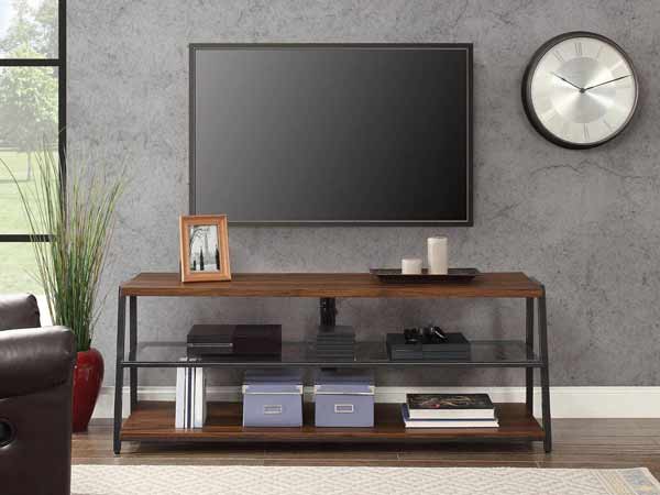 یک میز تلویزیون فلزی با ترکیبی از لایه چوبی به رنگ قهوه ای تیره می باشد و صفحه نمایشگر بالای میز به دیوار پشتی طوسی رنگی که دارد متصل شده است و یک ساعت در کنار تی وی دیده می شود. و یک قاب عکس و دو عدد شمع نیز روی میز تی وی قرار دارد.
