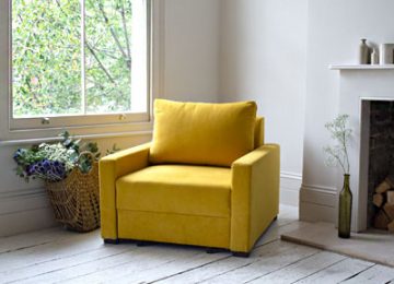 تصویر یک صندلی تختخواب شو زرد رنگ در فضای دکوراسیون منزل در کتار پنجره