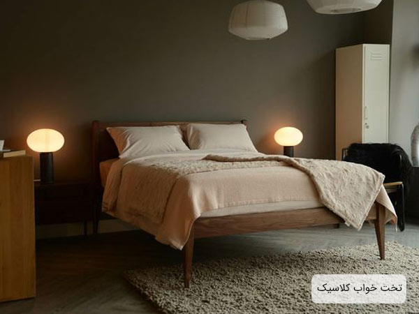 تختخواب چوبي قهوه اي رنگ مدل کلاسيک با يک عدد تشک سفيد و دو عدد آباژور رو ميزي که در کنار تخت قرار گرفته اند