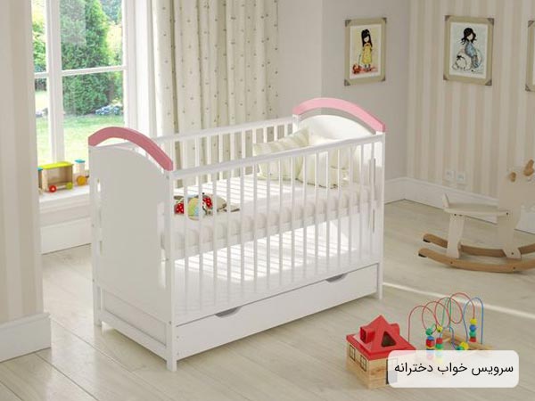 تخت خواب دخترانه مخصوص نوزاد با رنگ سفيد و صورتي که در اتاق خواب کودک قرار داده شده