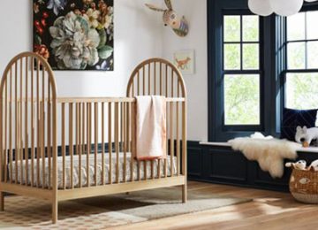 تصويری از يک تخت نوزاد کرمی رنگ چوبی که در اتاق خواب کودک قرار گرفته است .