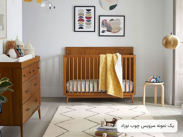 تصويری از سرويس خواب چوبی نوزاد به رنگ قهوه ای که شامل يک تخت نوزاد و يک دراور می باشد و اتاق خواب نوزاد با لوازم دکوری تزئين گشته است.