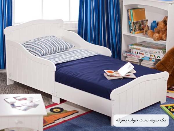 تصويری از يک تخت پسرانه با بدنه ای به رنگ سفيد و خوشخوابی به رنگ های آبی تيره و سفيد که يک عدد کتاب داستان کودکانه روی تخت قرار گرفته است.