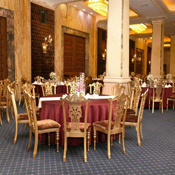 ميز ناهار خوری سلطنتی سپهر به رنگ طلايی و رو ميزی هايی قرمز رنگ به همراه چند صندلی ناهار خوری سلطنتی که دور اين ميز قرار داده شده اند.