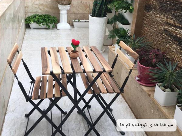 ميز و صندلی ناهار خوری چوبی به رنگ کرمی روشن در ابعاد کوچک که در کنار چند گلدان قرار گرفته است