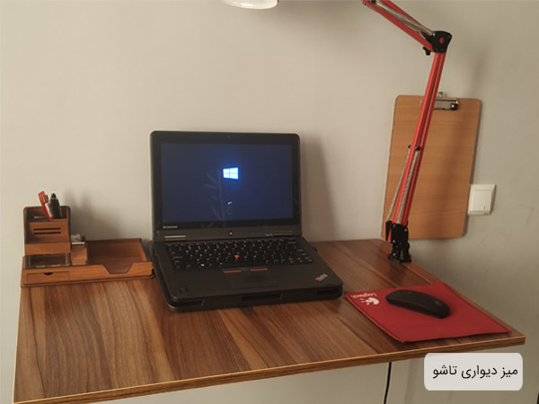 ميز تحرير کاردينو مدل غزال به رنگ قهوه ای که يک عدد لپ تاپ و يک جامدادی چوبی به همان در کنار يک چراغ مطالعه بر روی ميز قرار گرفته است.