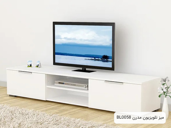 میز تلویزیون BL0058 به رنگ سفيد به همراه يک عدد تلويزيون و چند وسيله دکوري شامل يک گلدان در محيطي با دکوراسيون مدرن.