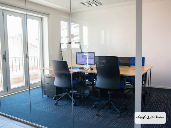 اتاق یک اداره با فضای محدود که دارای یک میز کار اشتراکی با صندلی های اطرافش است با دکوراسیون ساده و مینیمال.