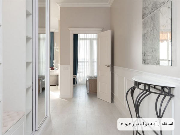 يک راهروی باريک با دکوراسيون مدرن و تم رنگی سفيد با يک آينه بزرگ و تابلو ديواری شيشه ای برای دکور.