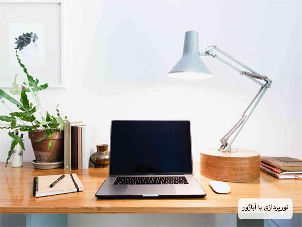 یک میز کار اداری با یک لپ تاپ و آباژور رومیزی برای نورپردازی.